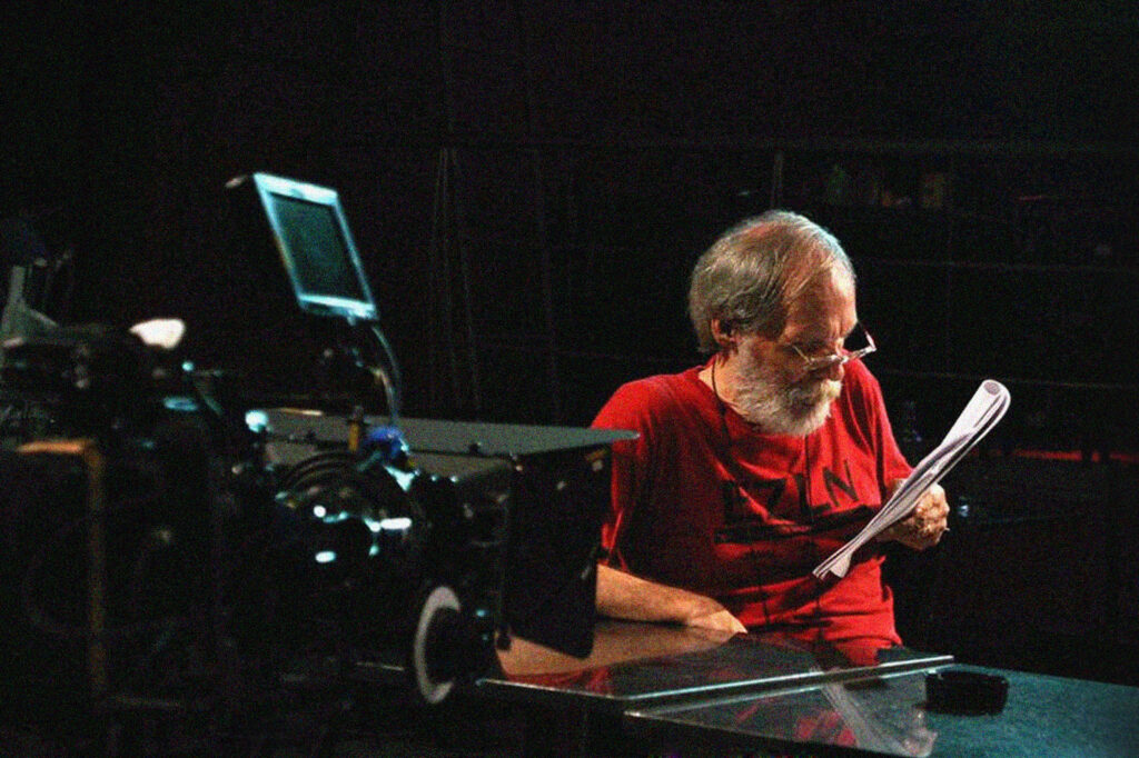 Imagem de Carlos Reichenbach em sua mesa lendo um roteiro em várias folhas de papel